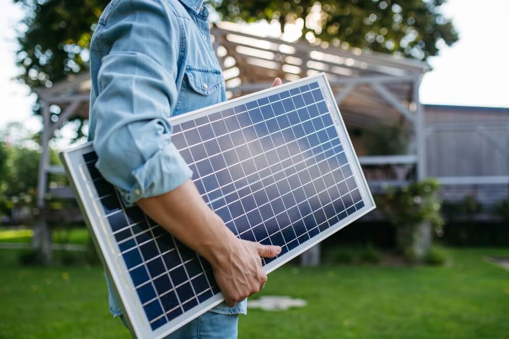 Man looking at the solar panel in his arms, standing in the garden