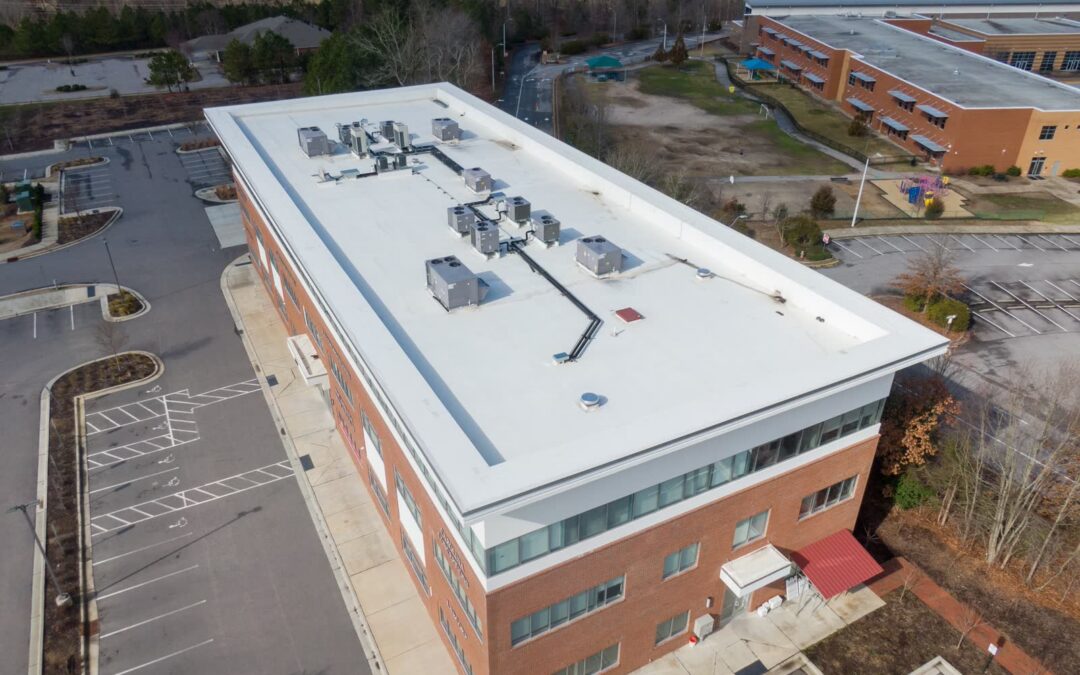Aerial view of a three-story brick office building with a white TPO membrane roof and rooftop HVAC units
