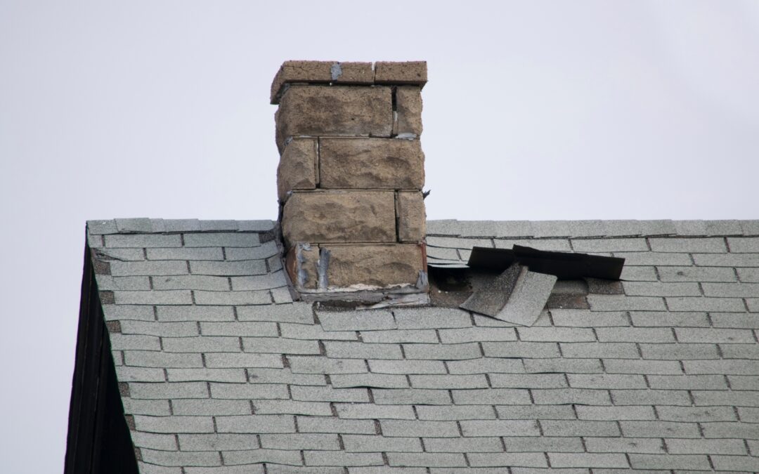 Damaged flashing and missing shingles at the base of a stone chimney on an asphalt shingle roof